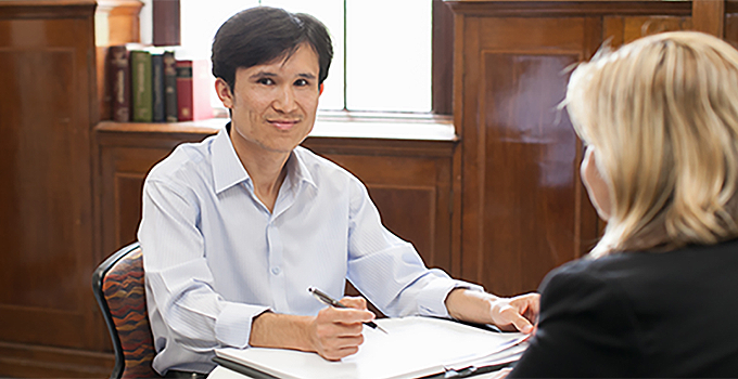 image of two people conversing while sitting at a table with documents