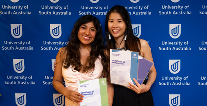image of two students in front of UniSA logo banner, holding leadership certificates