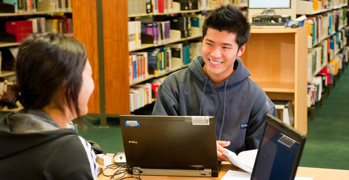 Image of two students on laptops in the library