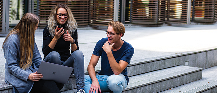 Three students with laptop and phone chatting together