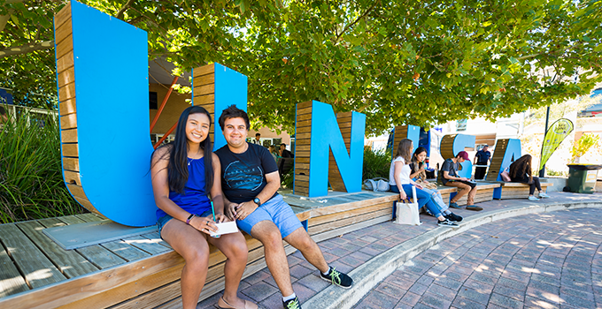 Image of students sitting on the 'UniSA' signage at Mawson Lakes campus
