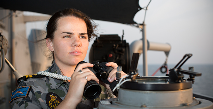 Image of woman in navy uniform, looking out to sea holding binoculars