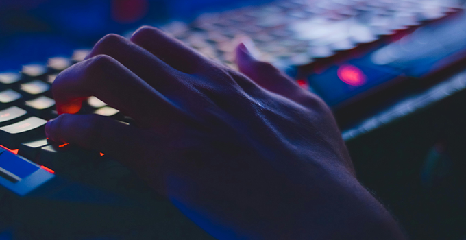 Darkly lit macro photograph showing hand typing on backlit keyboard.