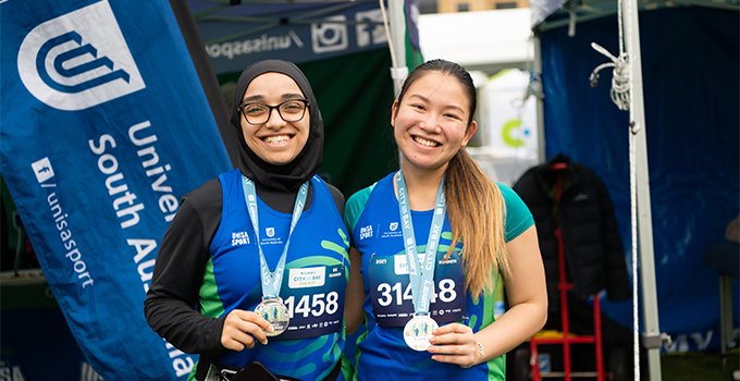 Two female UniSA students holding medals after participating in City-Bay Fun Run.