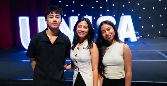Photo of three smiling students standing in front of illuminated UniSA signage lights
