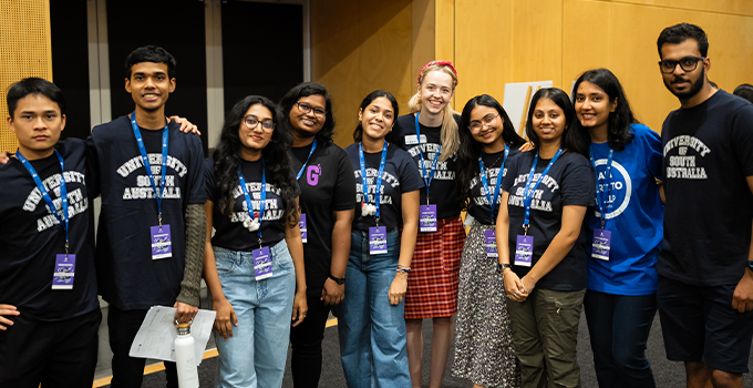 Group of UniSA volunteers in an indoor setting posing for camera and wearing UniSA branded shirts.