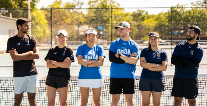 Image of male and female students at a tennis court wearing their team sport uniform