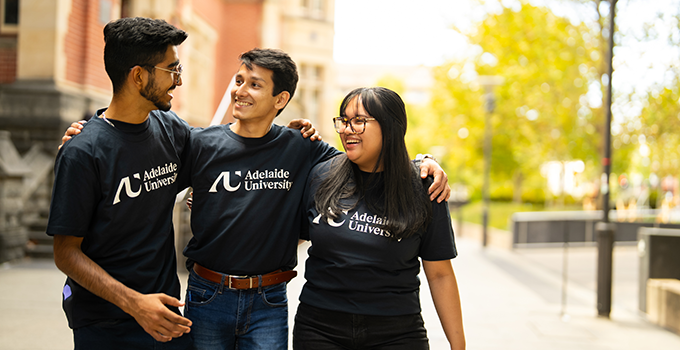 Two male and one female students wearing Adelaide University t-shirts on North Terrace.