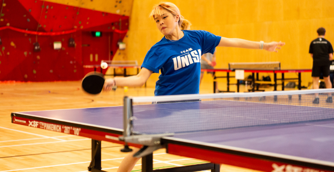 Female student wearing a blue Team UniSA shirt plays table tennis at Pridham Hall