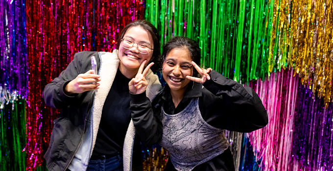 Image of two female students smiling at the camera with a colourful tinsel backdrop