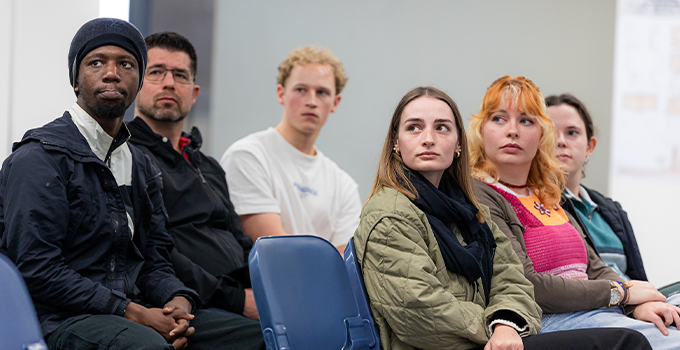 Group of students sitting in a classroom setting, watching something intently off screen. 