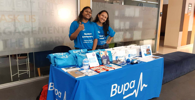 Two female Bupa Ambassadors behind Bupa drop-in stall