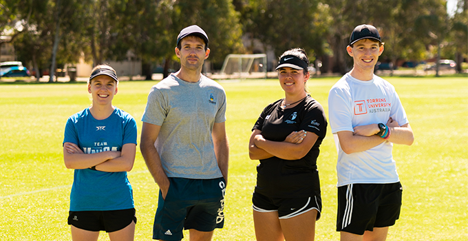 Image of four athletes standing on a soccer field, representing different University's with branded tees.