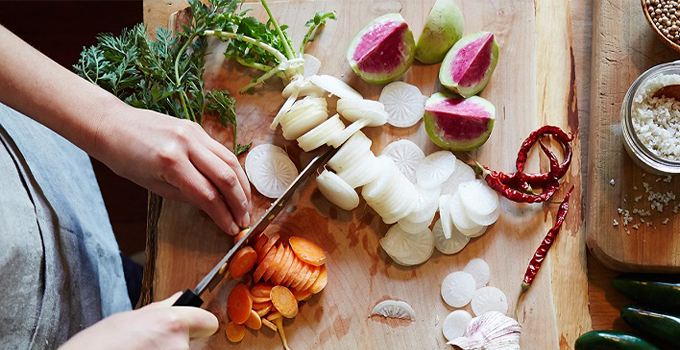 Close up photographic shot of hands cutting various vegetables on a cutting board.