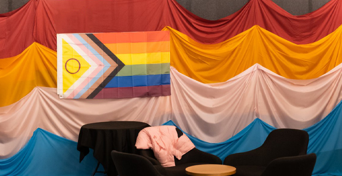 Progress pride flag displayed against multicoloured curtain