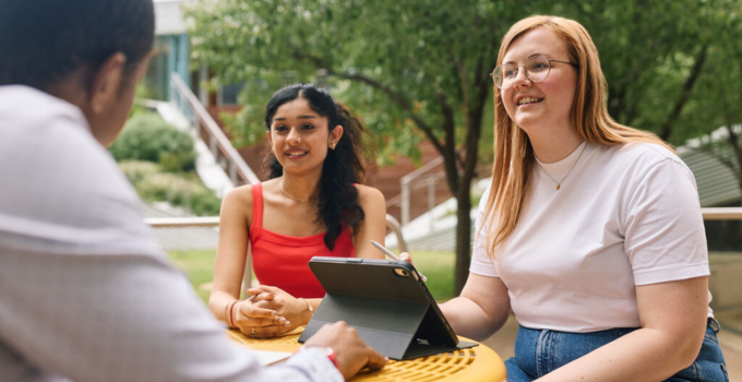 Photo of students having a discussion while learning on their laptop