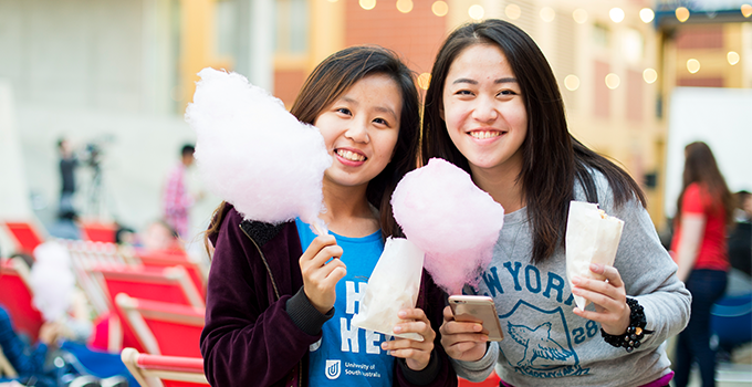 Two female students holding fairyfloss and popcorn at movie night event.