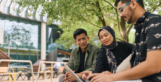 Photos of three students having a chat on campus while checking something on a laptop