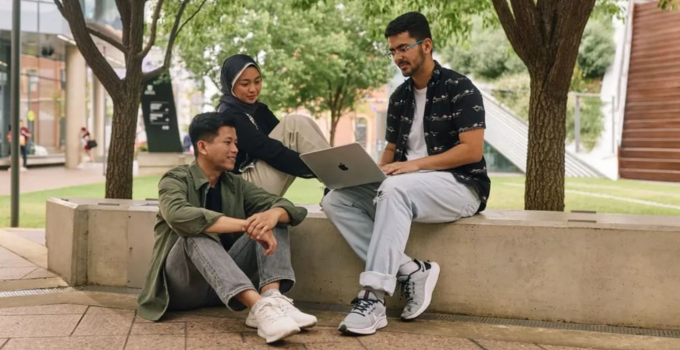 Three students looking at a laptop while outside at Hoj Plaza.