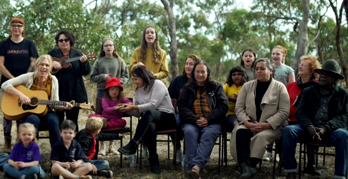 Group of children and adults performing song outdoors in a bush setting