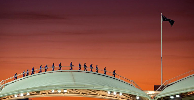 Wide angle view of participants on an Adelaide oval roof climb climb, against a sunset background.  
