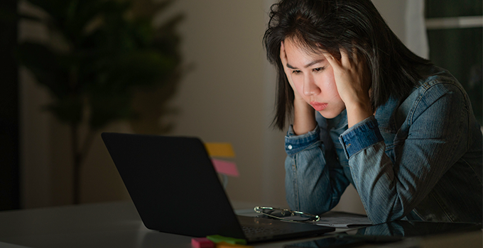 Stressed female student in dark room looking at laptop