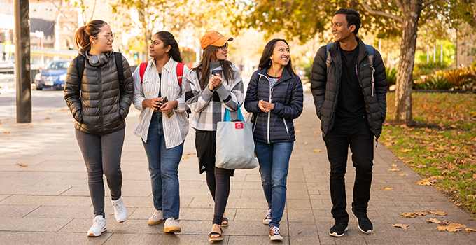 Image of four female and one male students walking along a footpath while chatting