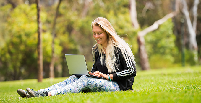 Female student working on laptop, sitting on Magill Campus lawn