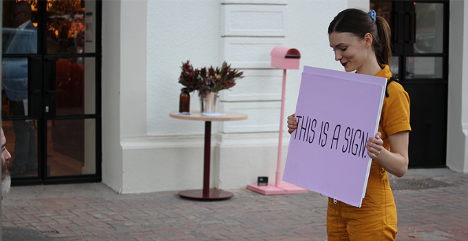 Image of woman holding a pink sign reading 'THIS IS A SIGN'