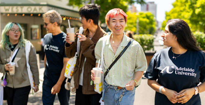 Group of five students chatting while walking along Hindley street. Two are wearing Adelaide University T-shirts.