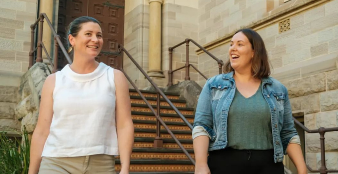 Photo of two female students smiling and walking confidently on campus