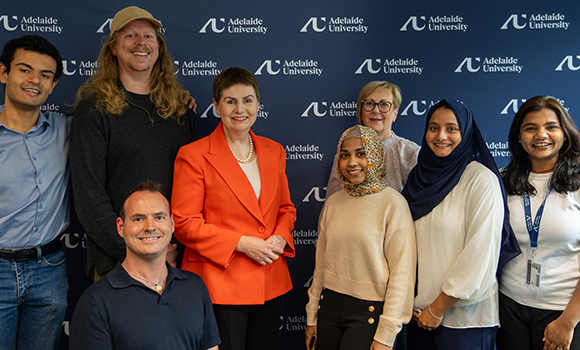 Photo of a group of smiling student panellists and staff from the Adelaide University Student Advisory Panel, in front of an Adelaide University backdrop
