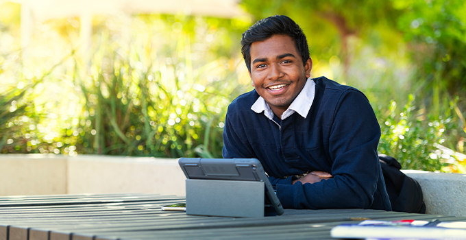 Photos of a male student sitting outdoors at a table with a tablet, smiling at the camera