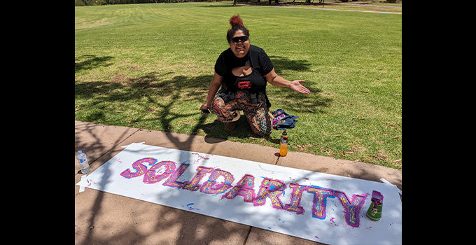 Artist Shania Richards displaying banner with painted text reading "Solidarity."